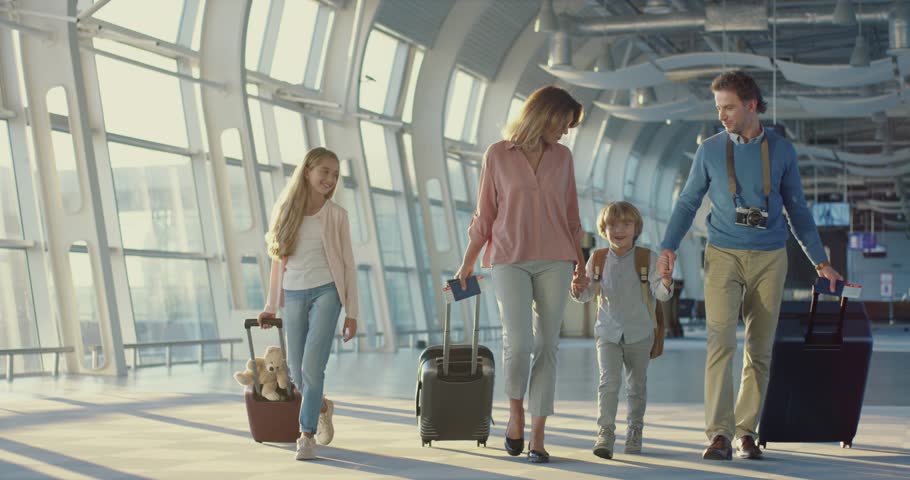 Caucasian happy mother, father, little daughter and son walking the airport hall and carrying their suitcases on the wheels before the departure to the vacation and laughing cheerfully  Royalty-Free Stock Footage #1026000557