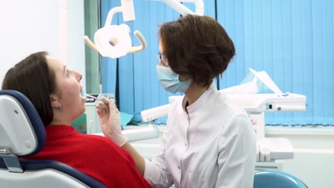 Girl dentist finishing to examine the oral cavity of the patient woman sitting in the dental chair, dental care concept. Young dentist in labcoat and a mask while treatment process. 庫存影片
