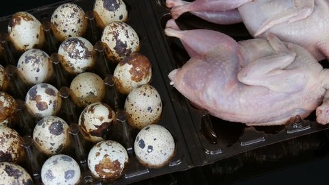 Fresh meat of quail in a plastic brown tray next to the quail eggs on a black background