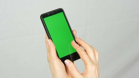 Well-groomed neat female hands with a beautiful manicure hold a black smartphone with a green screen or chrome key on a white background in the studio.