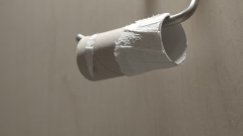 Close shot of mans hand reaching out to an empty toilet roll in frustration.