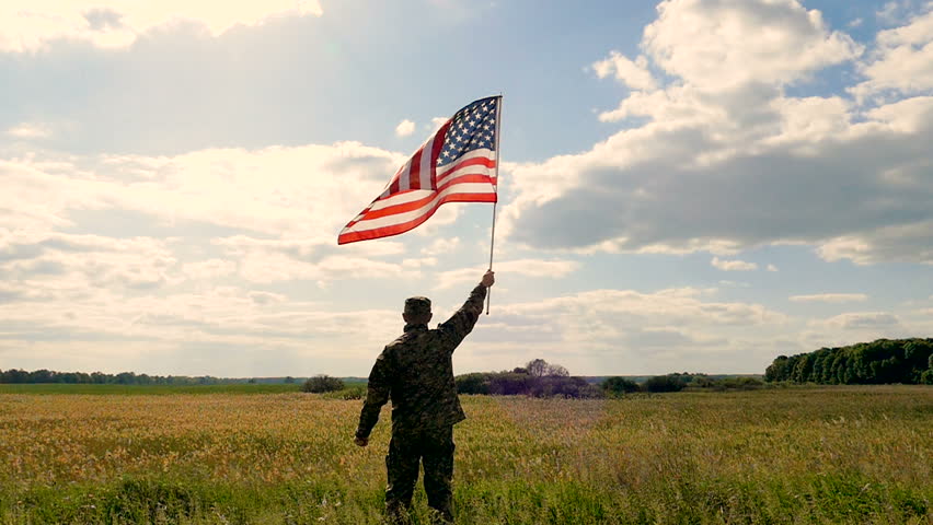 Soldier lifted up American flag against blue sky. Outdoor slow motion scene