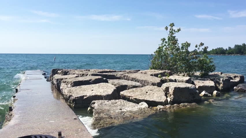 Waves and splashes on rocks at Woodbine Beach, Lake Ontario. Tree on the rocks. Stationed camera.