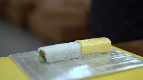 A close up video of roll preparation. A cook ends a slice of cheese and puts it on the roll.Then he squeezes it using rolling mat and tries to make everything tight. The background is blurred.