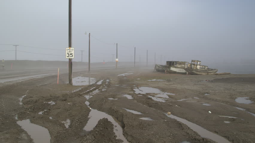 Cars driving on a misty coastal road next to wrecked boats at Barrow, Alaska