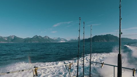 Back view of fishing boat with fishing rods and mountains in the background while sailing through the Gulf of Alaska