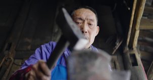 Close up low angle view of One senior Asian blacksmith working in the shop, strike a hot red metal with a hammer, traditional craftsman working in workshop slow motion clip