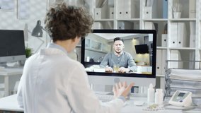 Back view of female Caucasian physician sitting at computer and talking to sick man about his cough by video link