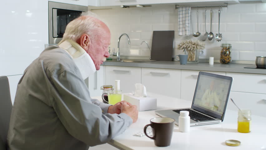 Medium shot of coughing aged patient with neck brace receiving online medical consultation