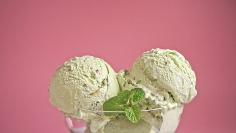 scoops of pistachio ice cream pouring chocolate glaze on pink background, slow motion