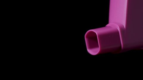 Pink asthma inhaler with spray coming out on black background. Slow motion 25%.