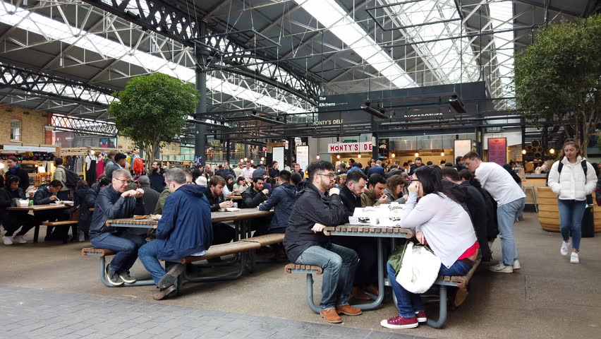 OLD SPITALFIELDS MARKET, LONDON - MARCH 20, 2019: Customers sit at benches to consume street food purchased from multiple kitchens inside Old Spitalfields Market in East London, UK.