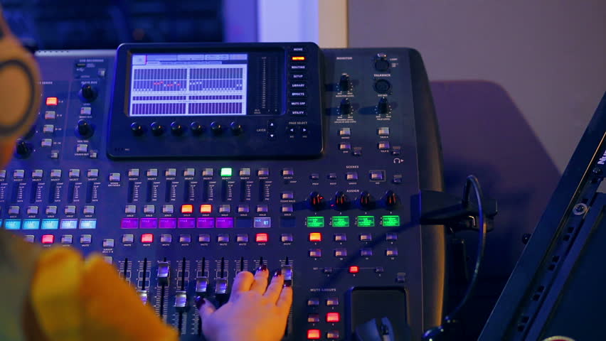 Woman DJ in headphones behind a mixing console working in color lighting | Shutterstock HD Video #1026068816