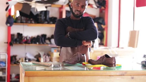 Young African cheerful shoemaker in workshop. Looking at camera.