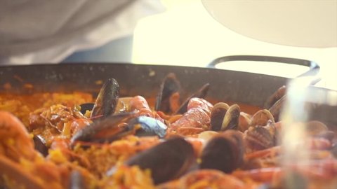 Paella traditional Spanish food. Person putts seafood paella from the fry pan to plate. Paella with with mussels, king prawns, langoustine and squids. Person cooking paella. Dinner. Slow motion 4K