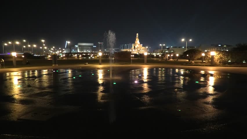 Colorful water fountain at Souq Waqif Park at Doha Corniche with Fanar Islamic Cultural Center and Minaret at night on background. Doha center in Qatar, Middle East, Arabian Peninsula in Persian Gulf.