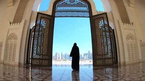 Woman with abaya dress looks at views of skyscrapers of Doha West Bay skyline outdoors State Grand Mosque in Doha, Qatar, Middle East, Arabian Peninsula.