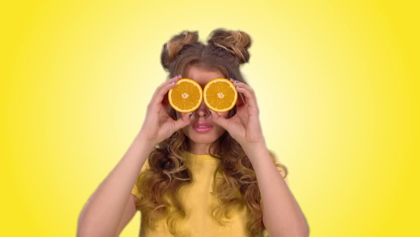 attractive girl in a yellow vest closes her eyes with oranges and smiles looking into the camera