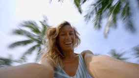 Young woman taking selfie under palm tree on vacations having fun enjoying tropical holidays; caucasian female capturing self portrait in exotic destination turning around quickly   