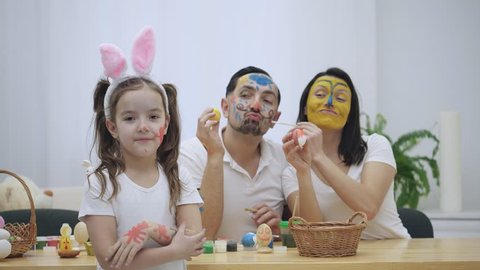 Cute couple is colorizing each other with a help of Easter paint-brush. Their daughter says: "Shame on you I have grown up, but neither you ". Childish couple came back to childhood.