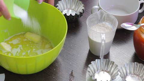 A woman adds flour and sugar to a container of melted butter. Begin to knead the dough for cooking cakes.