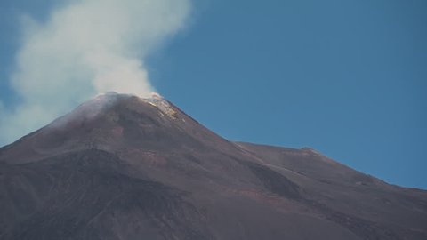 Pan across volcanic lava flows to see the smoking cone of Mount Etna, Sicily
