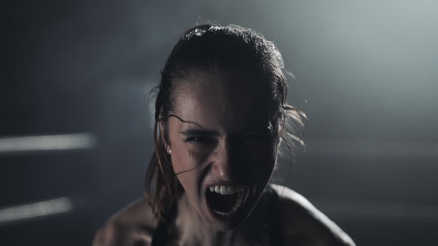 Portrait of tired female boxer standing on the boxing ring, looking intensely at the camera and screaming
