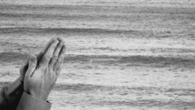 Repeatable loop video of praying hands with a calm sea in the background with a pencil sketch effect