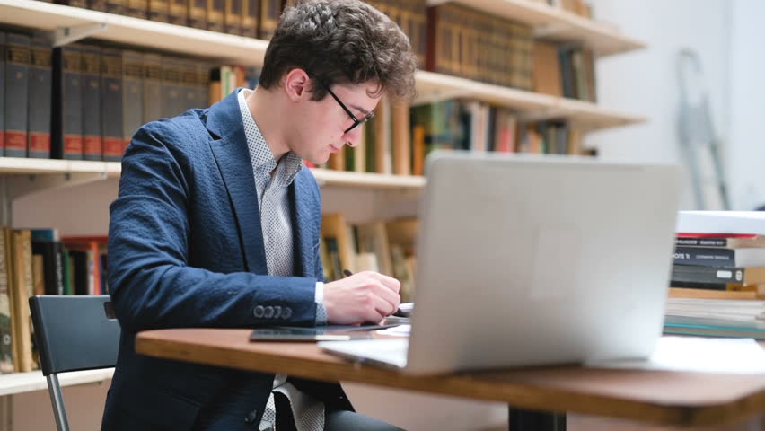 Students studying over desktop computers while sitting at table in library using digital tablet – learning, researching, knowledge concept