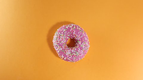 Various colorful donuts in stop motion on orange background. Top view