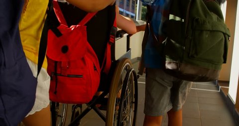 Rear view of group of diverse schoolkids pushing disabled Caucasian schoolgirl in wheelchair at corridor. They are interacting with each other
