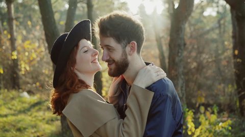 Happy man put hat on female head and embraces her in sunny park. 4K