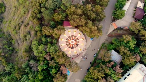 Hypnotic aerial view of spinning carousel in amusement park in Tbilisi, Georgia. People riding the chairoplane carousel and having fun at the funfair. Taken by drone.