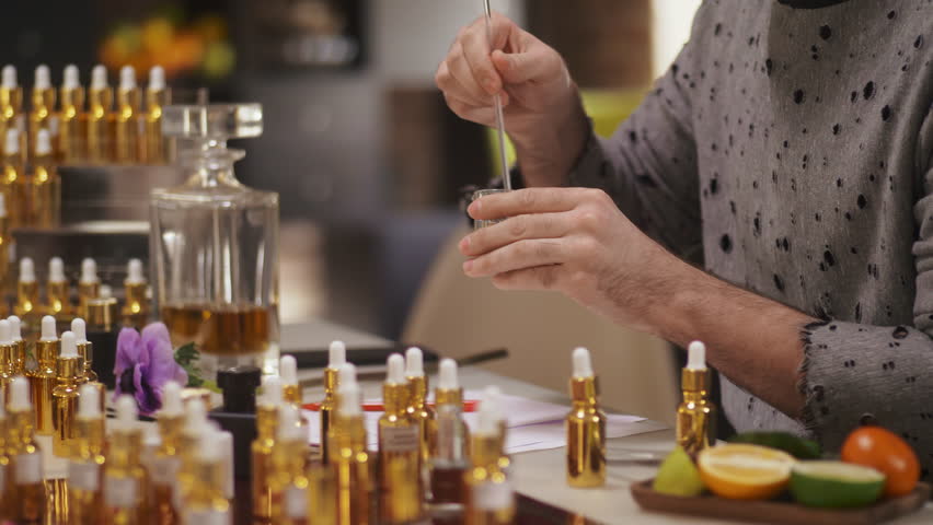 Portrait of young man blending scents for new perfume sitting at his desk full of bottles and samples at workshop Royalty-Free Stock Footage #1026133604