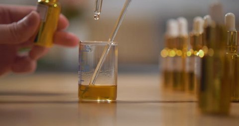 Close up of perfumer adding essential oil into alcoholic mixture in test-tube