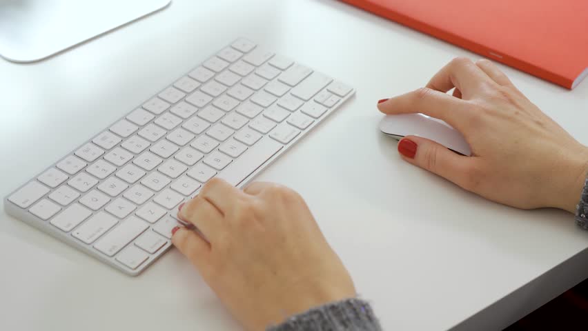 Female hands with red nails use mouse and typing on white computer keyboard