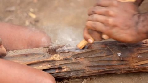 The smog is coming from the wooden log while the tribal man is trying to get the spark by rubbing the stick. The historical method of inflating the flames showed by Vanuatu aborigines.