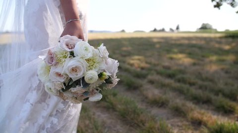 Bride holding beautiful floral bouquet wearing wedding dress in a grassy field at golden hour Stockvideó