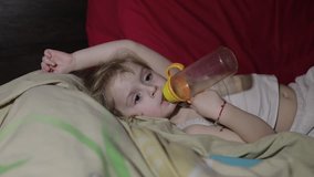 Young girl watching tv television on the bed and drinks a juice from a bottle. Kid hypnotized by screen watching content. Child in hypnosis state