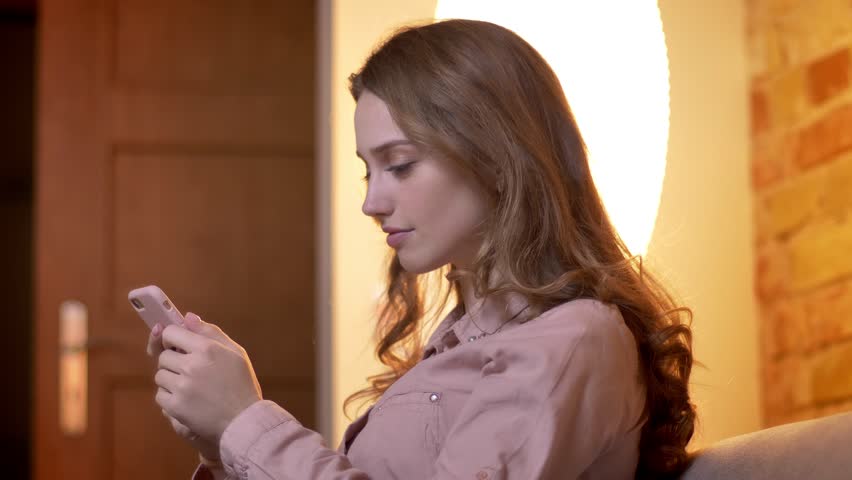Profile portrait of young teenage girl watching into smartphone turns to camera and smiles in cozy home atmosphere. | Shutterstock HD Video #1026147353