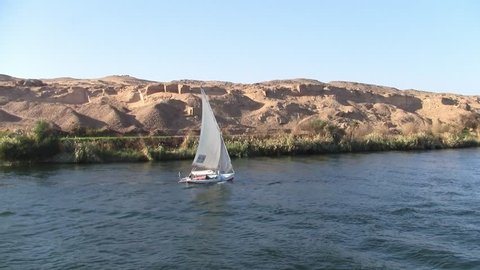 Traditional White Felucca Sail Boat on the River Nile with an Arid Desert Landscape as a Background