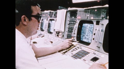 1960s: Men in front of monitor in NASA mission control room. Men in mission control. Hand writing in book. People sitting at monitors. People looking over data on paper.