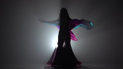 Woman with a veil in her hands dancing belly dance. Sihouette . Black smoke background. Slow motion