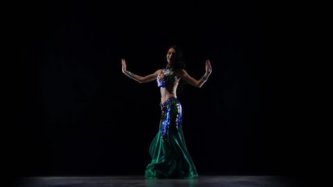 Girl performing a belly dance in dark studio. Black background. Slow motion