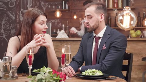 Young, adorable couple at a romantic dinner date. Young man dressed in a suit talks with his beautiful girlfriend.