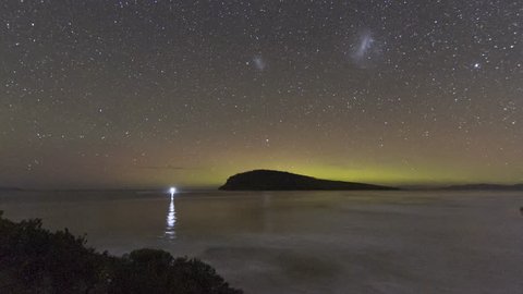 The Aurora Australis or Southern Lights dancing in the sky behind an island in the ocean, Tasmania. 