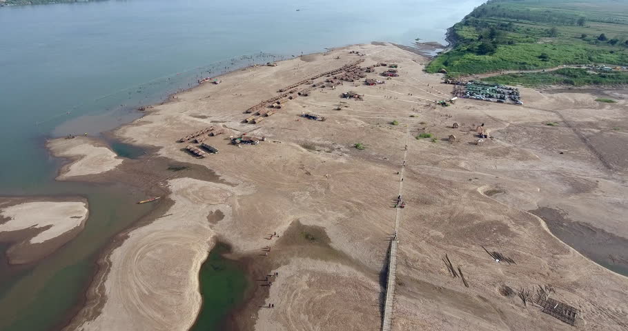 overhead drone of straw huts and wooden bungalows spread over sand beach