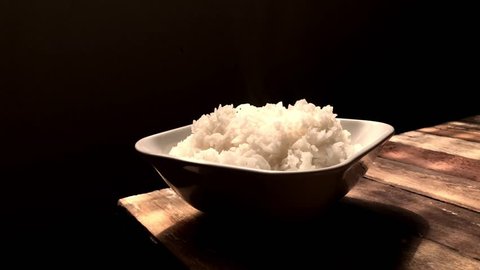 Professional chef,scoop parboiled rice put in a white bowl,steamed rice with smoke,on empty old wood,with space for text.Rustic still life,dark background,dimly light.