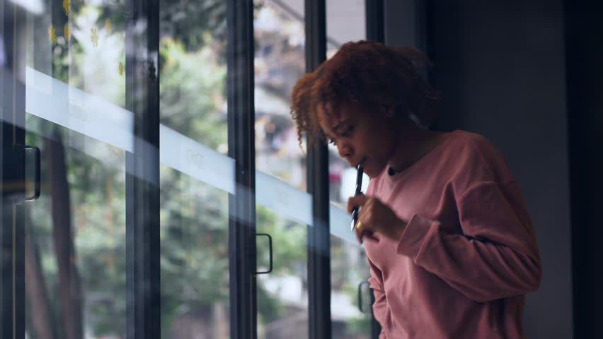 One pretty African young woman standing by the desk writing on the notebook in the cafe by the window. Beautiful Black freelancer using laptop  working indoor, young people working studying lifetyles