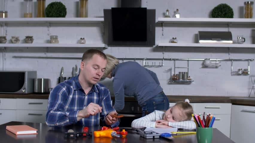 Bored preadolescent daughter expressing indifference during home craft lesson while father teaching on example of toy tool set how to tighten screws. Tedious for girls shop class in domestic kittchen. Royalty-Free Stock Footage #1026191189